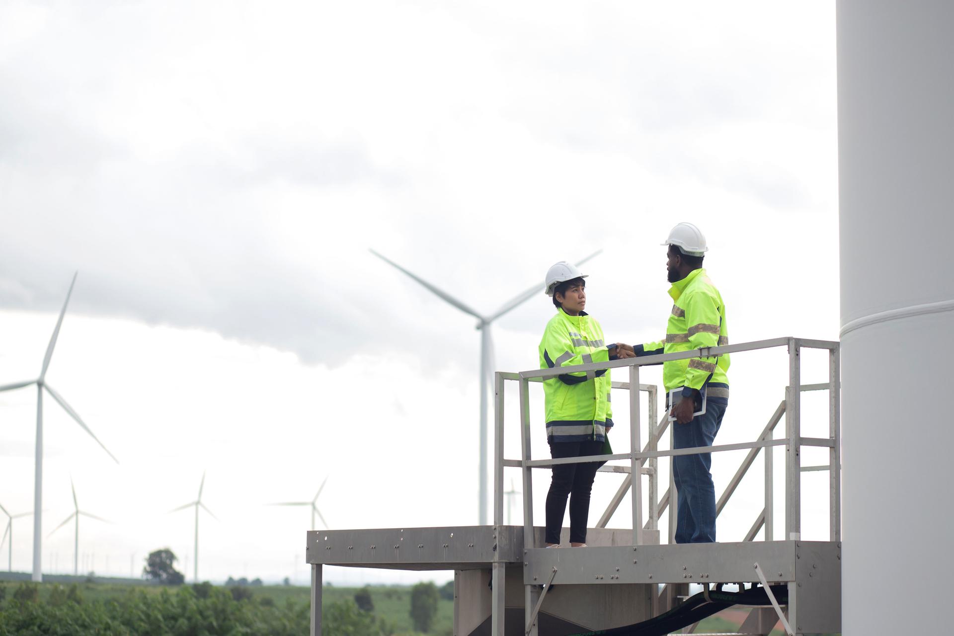 Two young engineer handshake about agreement of success renewable in wind turbines farm, renewable energy and sustainable collaboration for success and innovation, engineer shaking hands.