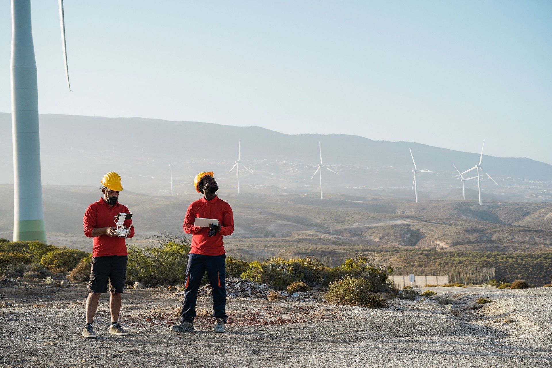 Multiracial engineer men working on windmill farm with digital tablet and drone - Renewable energy concept