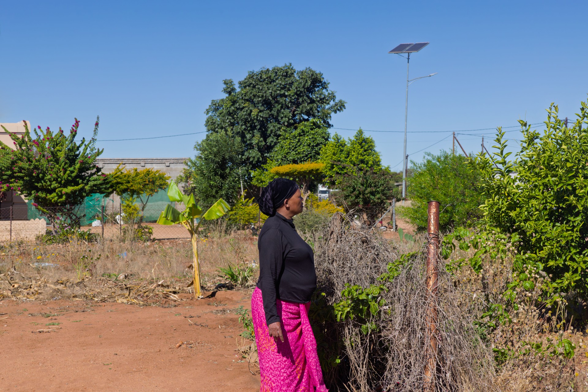 Africa village, single african woman, standing in the yard, renewable energy panel for illumination