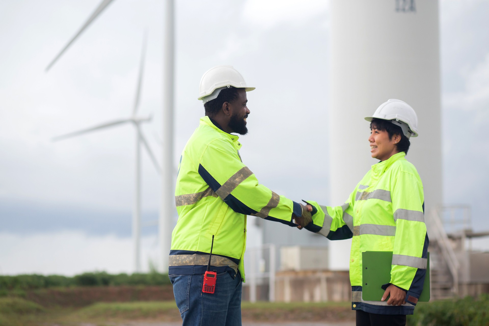 Two young engineer handshake about agreement of success renewable in wind turbines farm, renewable energy and sustainable collaboration for success and innovation, engineer shaking hands.